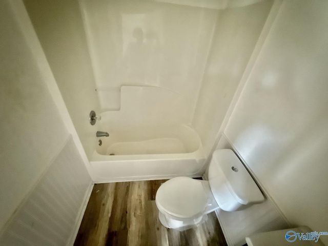 bathroom featuring wood finished floors, toilet, and bathing tub / shower combination