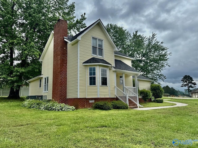 rear view of property with a chimney, a yard, a porch, and roof with shingles