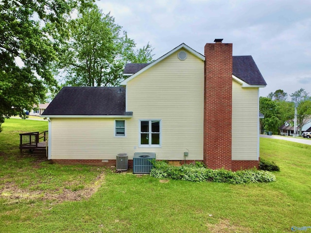 rear view of house with central AC, a shingled roof, a chimney, and a yard