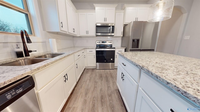 kitchen featuring sink, white cabinetry, hanging light fixtures, stainless steel appliances, and light hardwood / wood-style floors