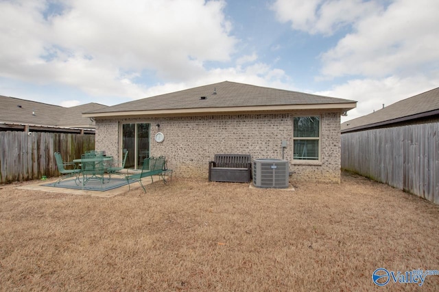 rear view of property with central air condition unit, a fenced backyard, a yard, brick siding, and a patio area