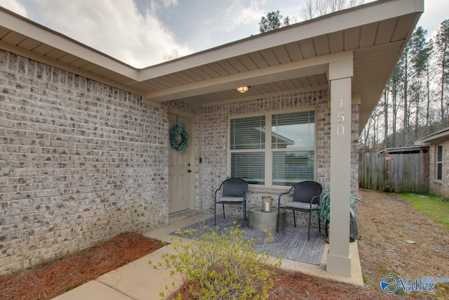 view of exterior entry with fence and brick siding