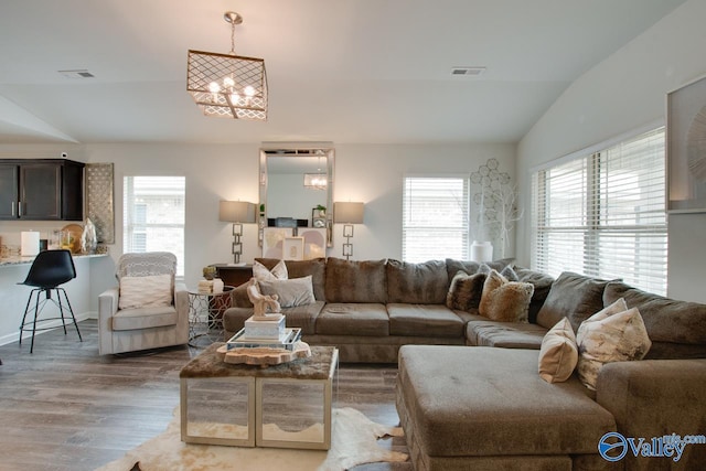 living area featuring visible vents, lofted ceiling, a notable chandelier, and wood finished floors