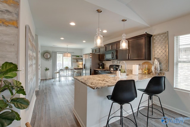 kitchen with range with electric cooktop, light wood-style floors, dark brown cabinetry, black microwave, and light stone countertops