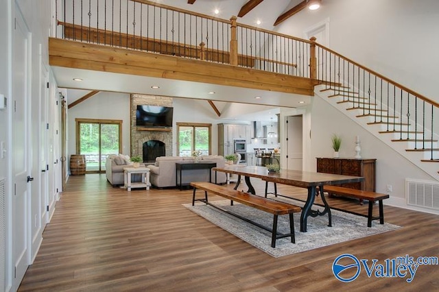 dining space with a high ceiling, a fireplace, stairs, wood finished floors, and visible vents
