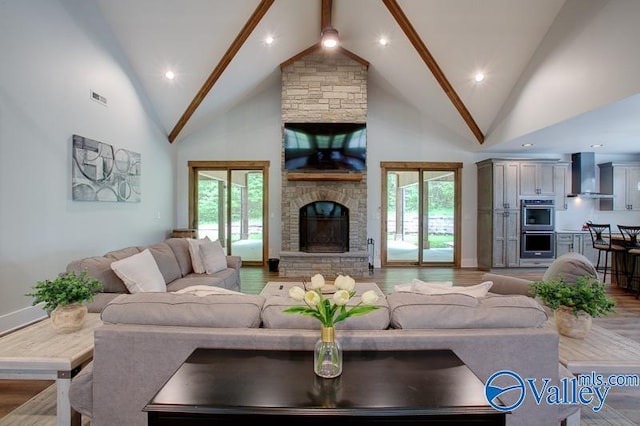 living area with visible vents, wood finished floors, a healthy amount of sunlight, a fireplace, and high vaulted ceiling