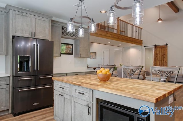 kitchen featuring high end black fridge, light wood-style flooring, wooden counters, and a barn door