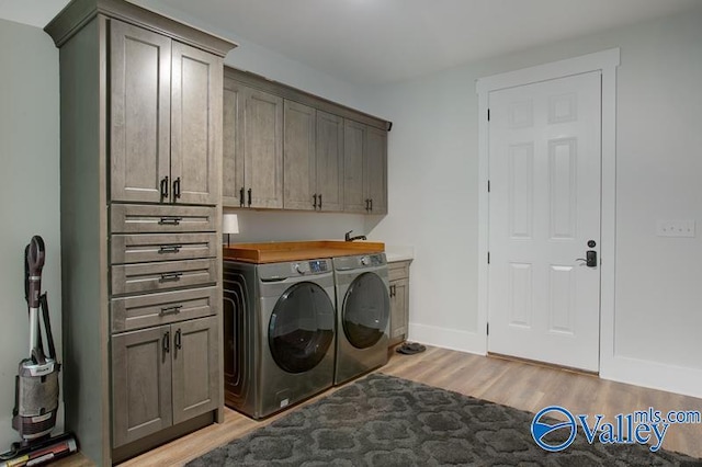laundry room featuring cabinet space, separate washer and dryer, baseboards, and light wood-type flooring