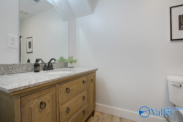 half bath featuring visible vents, vanity, wood finished floors, toilet, and baseboards