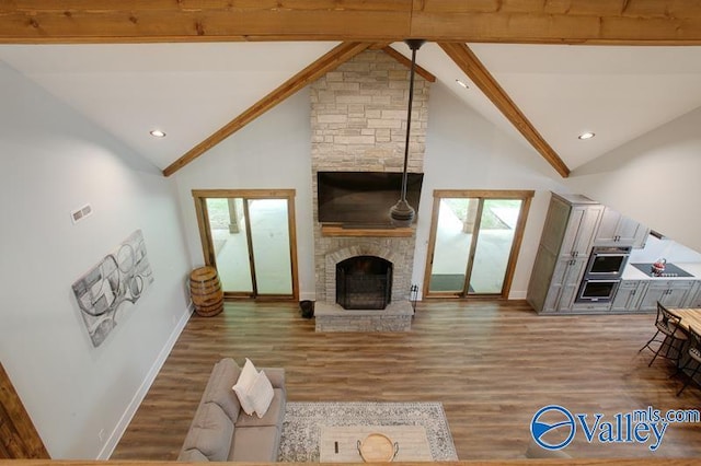 living area featuring a large fireplace, baseboards, beamed ceiling, and a wealth of natural light