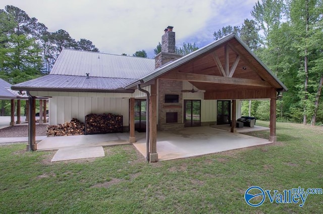 back of property with a lawn, a patio area, a chimney, and metal roof