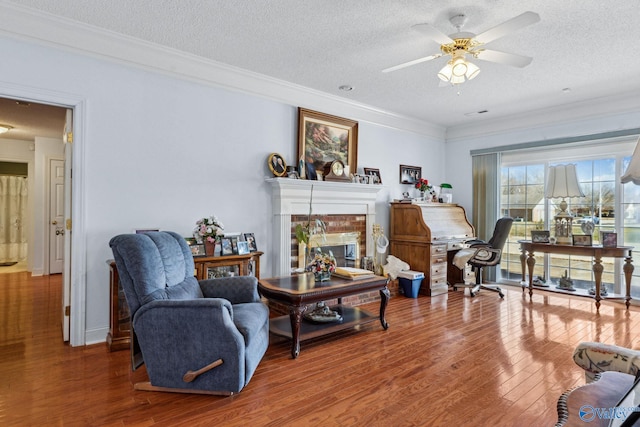 living area with a fireplace, wood-type flooring, ceiling fan, crown molding, and a textured ceiling