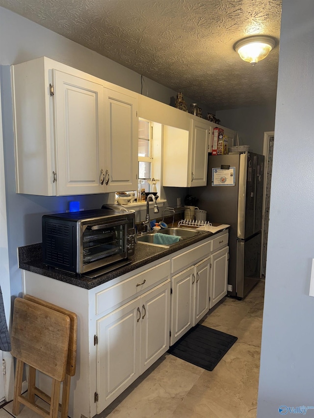 kitchen with dark countertops, a toaster, white cabinets, and a sink