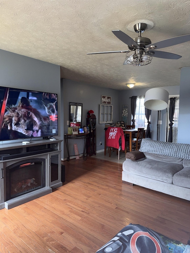 living room with ceiling fan, a fireplace, a textured ceiling, and wood finished floors