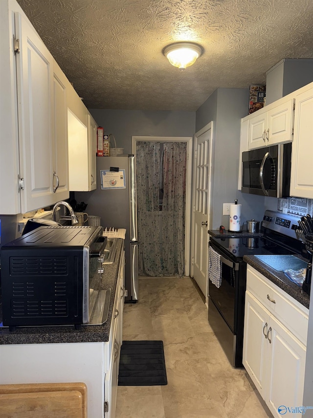 kitchen with appliances with stainless steel finishes, dark countertops, white cabinetry, and a textured ceiling