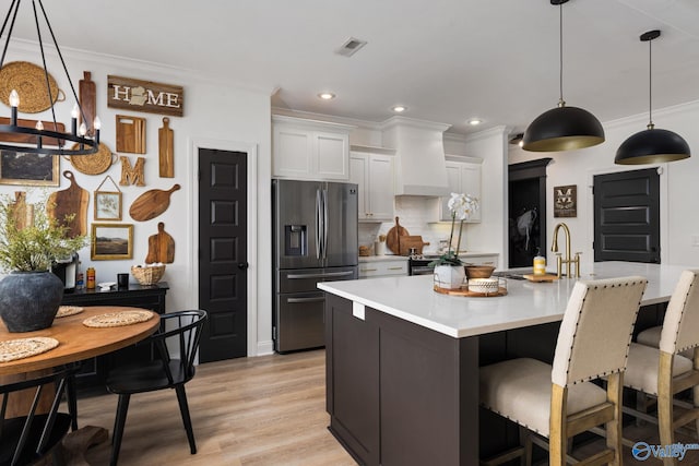 kitchen with a sink, stainless steel fridge, crown molding, and premium range hood