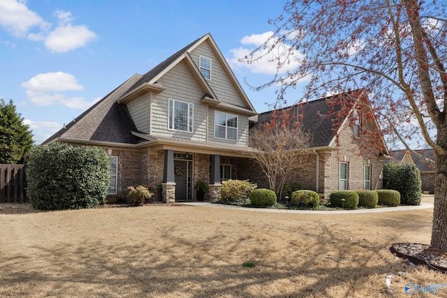 craftsman-style home with fence, brick siding, and a shingled roof