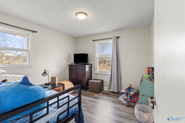 bedroom with a textured ceiling, wood finished floors, visible vents, and baseboards