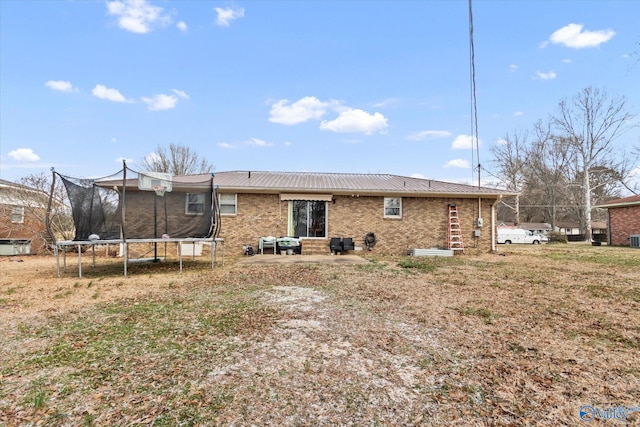 rear view of house featuring a patio area, a trampoline, metal roof, and brick siding