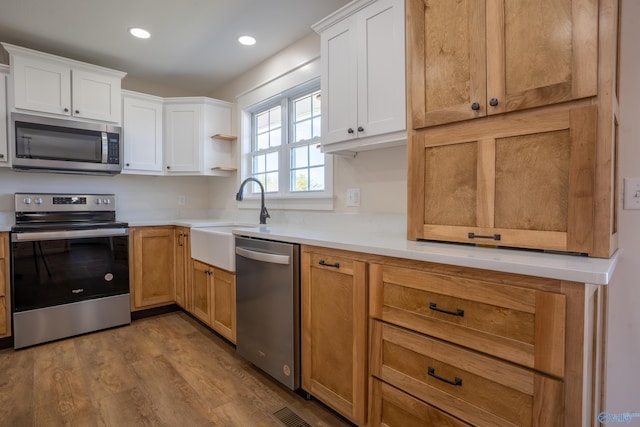kitchen with a sink, wood finished floors, white cabinetry, stainless steel appliances, and light countertops
