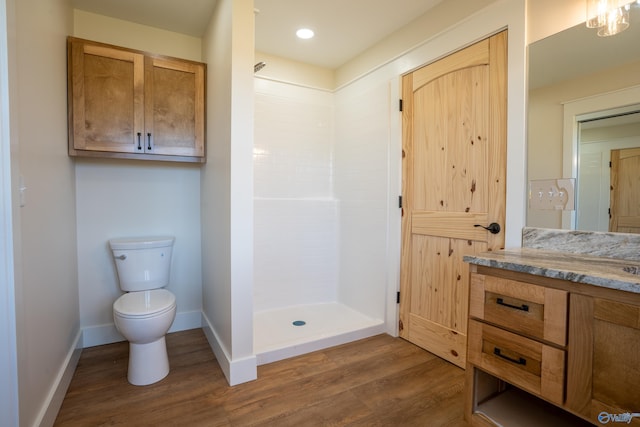 bathroom featuring toilet, wood finished floors, a tile shower, baseboards, and vanity