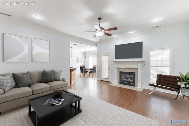 living room with ceiling fan, wood finished floors, visible vents, and ornamental molding