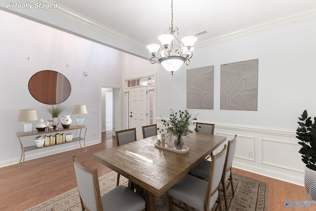 dining space with an inviting chandelier, crown molding, a decorative wall, and wood finished floors