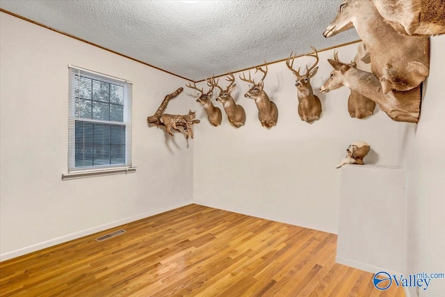 spare room featuring crown molding, a textured ceiling, and light wood-type flooring