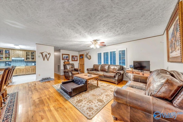 living room featuring a textured ceiling, light wood-type flooring, and ceiling fan