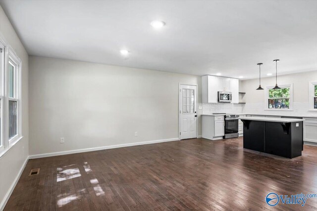 kitchen featuring hanging light fixtures, stainless steel appliances, a kitchen island, a kitchen bar, and white cabinets