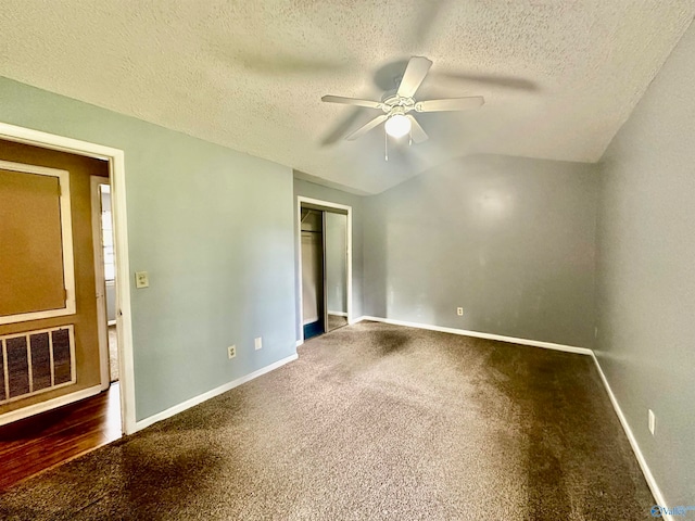 unfurnished bedroom with ceiling fan, a textured ceiling, dark colored carpet, and vaulted ceiling