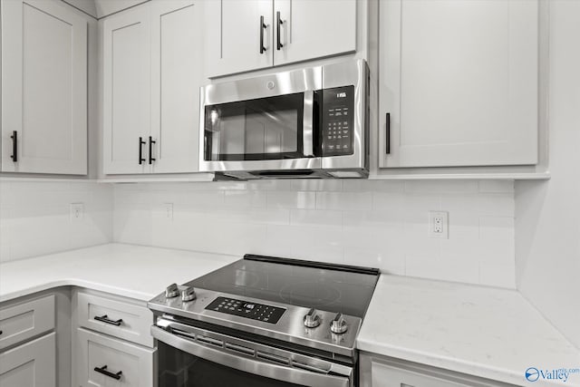 kitchen with decorative backsplash, white cabinetry, light stone counters, and appliances with stainless steel finishes