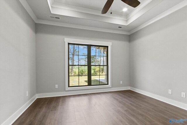 empty room featuring ornamental molding, dark hardwood / wood-style floors, ceiling fan, and a tray ceiling