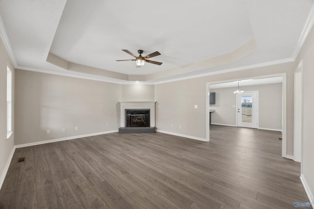 unfurnished living room with a brick fireplace, ornamental molding, ceiling fan with notable chandelier, dark hardwood / wood-style floors, and a tray ceiling