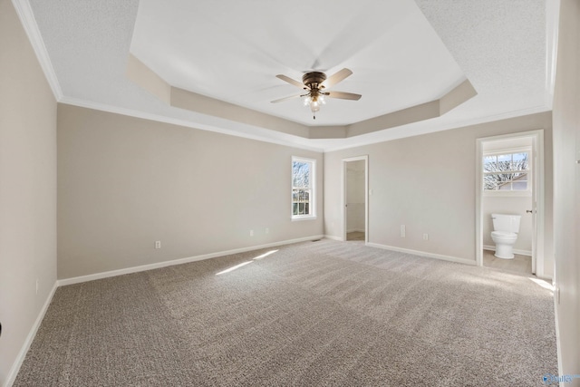 unfurnished bedroom featuring ceiling fan, ensuite bathroom, a raised ceiling, and carpet flooring