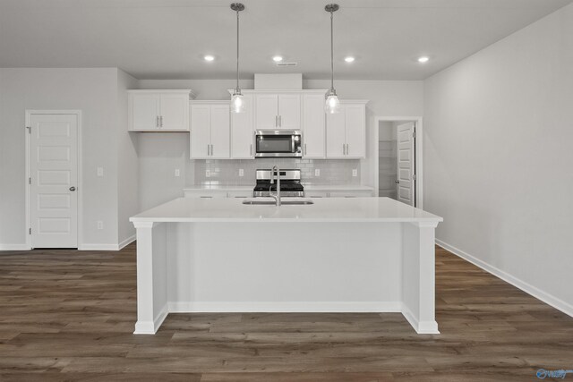 kitchen featuring dark hardwood / wood-style flooring, appliances with stainless steel finishes, a center island with sink, backsplash, and sink