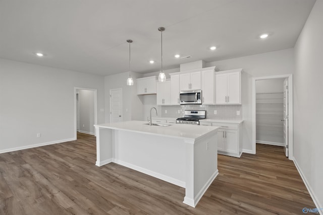 kitchen featuring dark hardwood / wood-style flooring, appliances with stainless steel finishes, an island with sink, backsplash, and sink