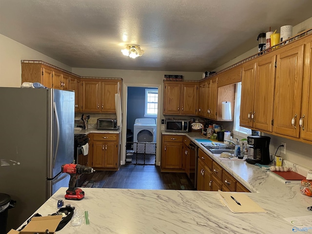 kitchen featuring dark wood-type flooring, appliances with stainless steel finishes, washer / clothes dryer, and sink