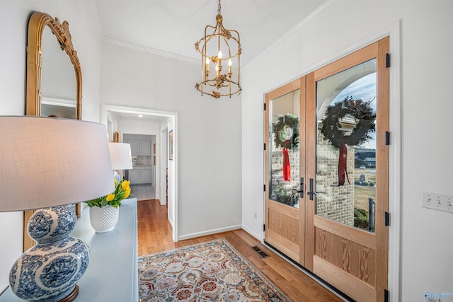 foyer featuring an inviting chandelier, ornamental molding, light hardwood / wood-style floors, and french doors