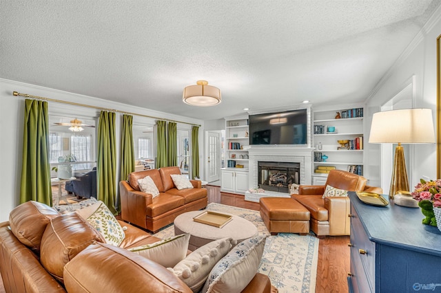 living room with ornamental molding, a textured ceiling, a brick fireplace, built in shelves, and light wood-type flooring