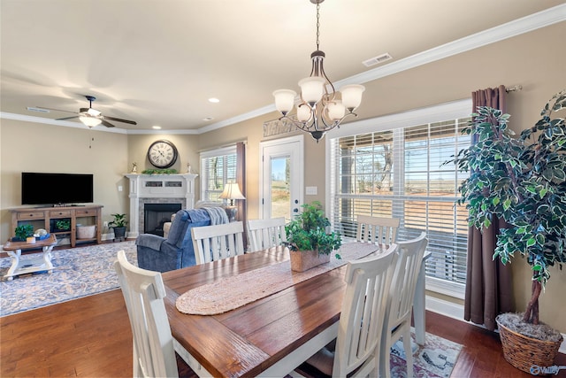 dining room with ceiling fan with notable chandelier, a fireplace, visible vents, dark wood-style floors, and crown molding