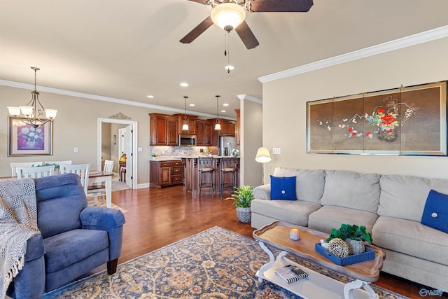 living area featuring dark wood-style flooring, recessed lighting, ornamental molding, baseboards, and ceiling fan with notable chandelier