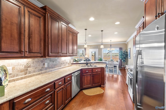 kitchen with wood finished floors, a sink, hanging light fixtures, appliances with stainless steel finishes, and crown molding