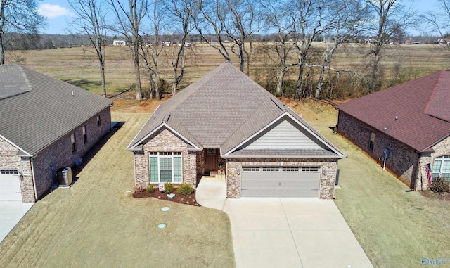 view of front of property featuring concrete driveway, roof with shingles, an attached garage, central air condition unit, and a front yard