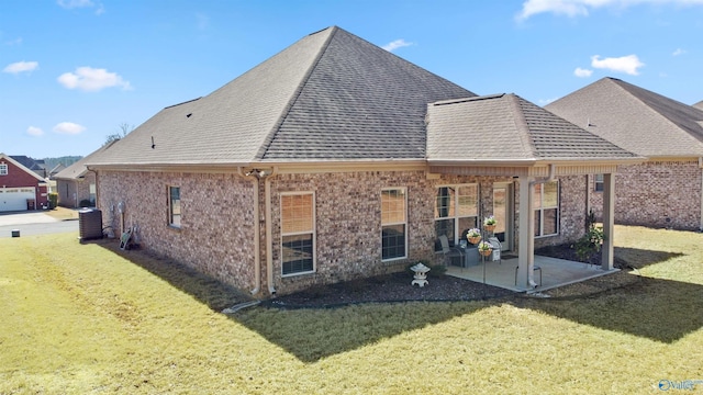 back of house featuring brick siding, a yard, central air condition unit, a shingled roof, and a patio area