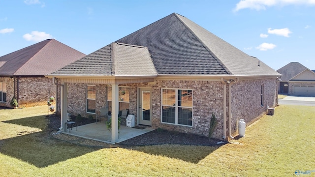 rear view of property featuring roof with shingles, brick siding, a lawn, and a patio