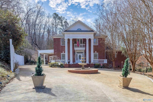 greek revival inspired property featuring a balcony, a porch, fence, and brick siding