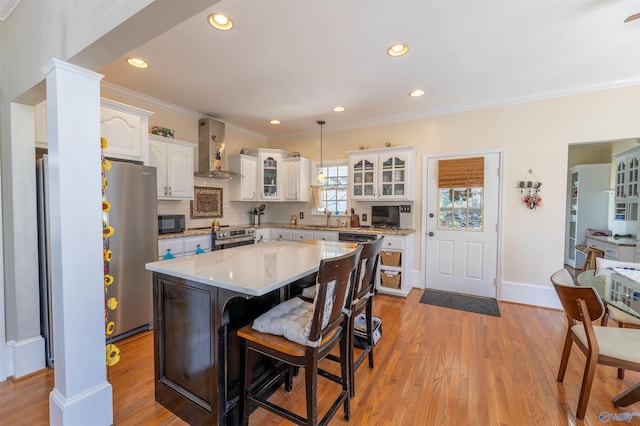 kitchen featuring a center island, decorative light fixtures, glass insert cabinets, white cabinetry, and wall chimney range hood