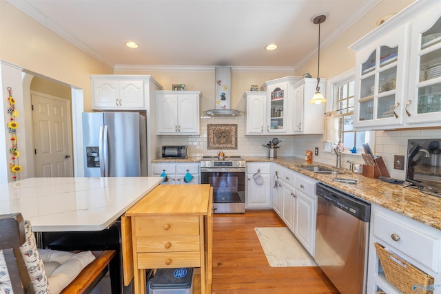 kitchen with wall chimney exhaust hood, glass insert cabinets, appliances with stainless steel finishes, a center island, and hanging light fixtures