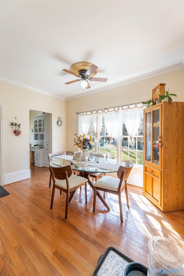 dining room featuring ornamental molding, light wood-style floors, baseboards, and a ceiling fan